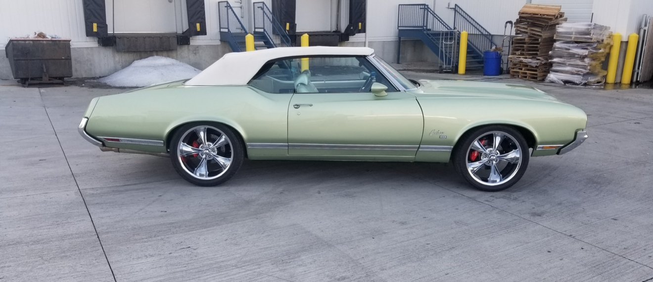 After: the same Cutlass Supreme convertible finished in light metallic green with a white top and polished five-spoke wheels, parked outside the shop