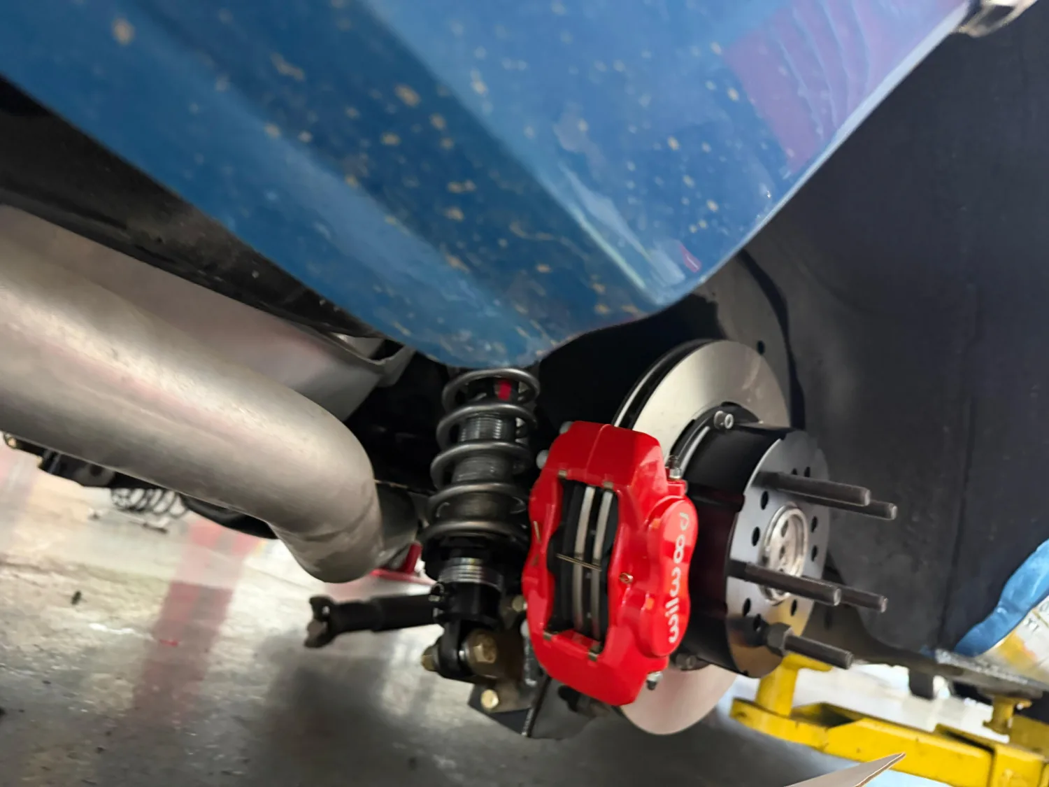 Rear suspension on a lifted car: a coilover shock, red four-piston brake caliper and vented disc, with polished exhaust running past